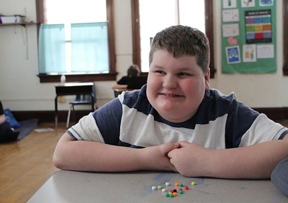 Student smiling while he plays with beads